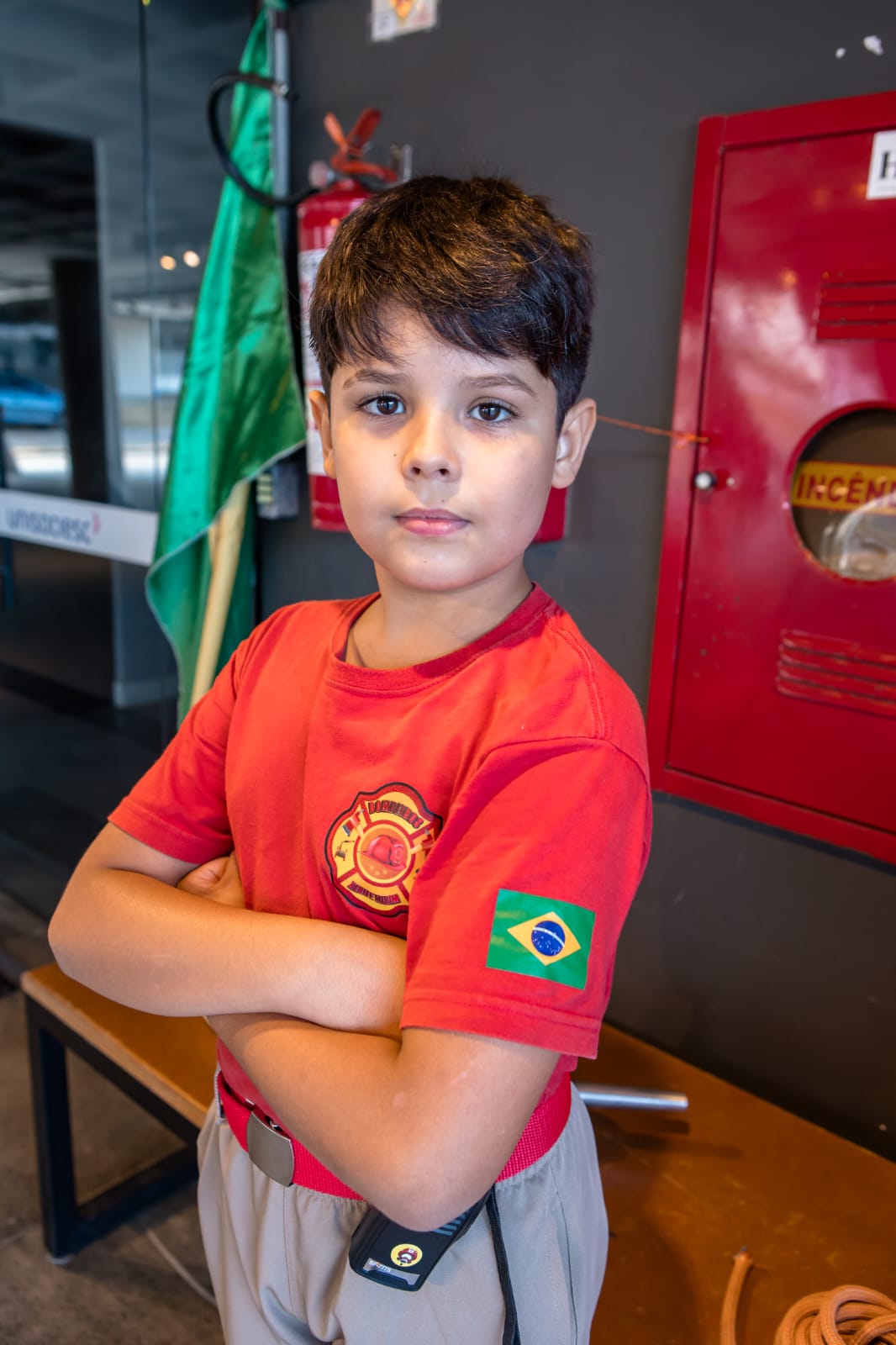 Bombeiro mirim de braços cruzados ao lado do extintor e do hidrante